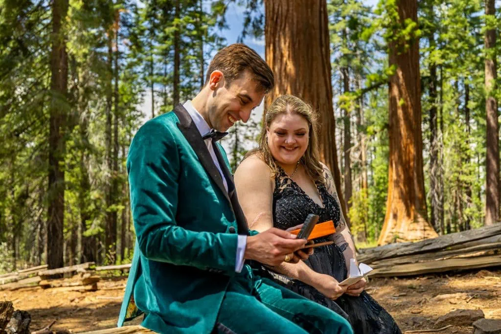 The offbeat bride and groom sit on a fallen log to read letters and open gifts from loved ones.
