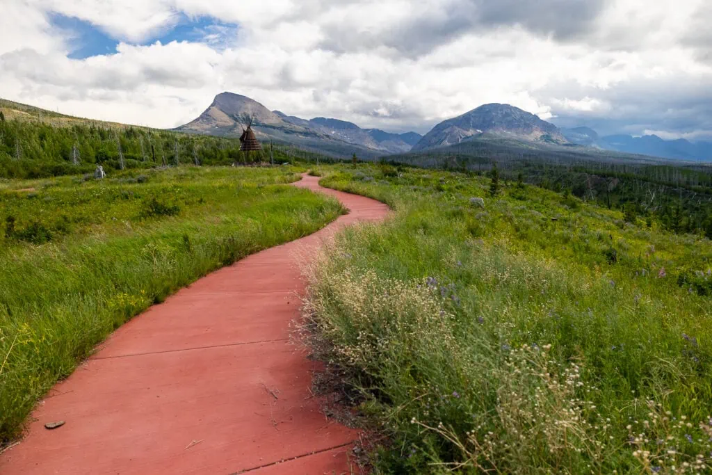 A red concrete path winds towards the mountains of Glacier National Park in northern Montana. This location is outside of the park.