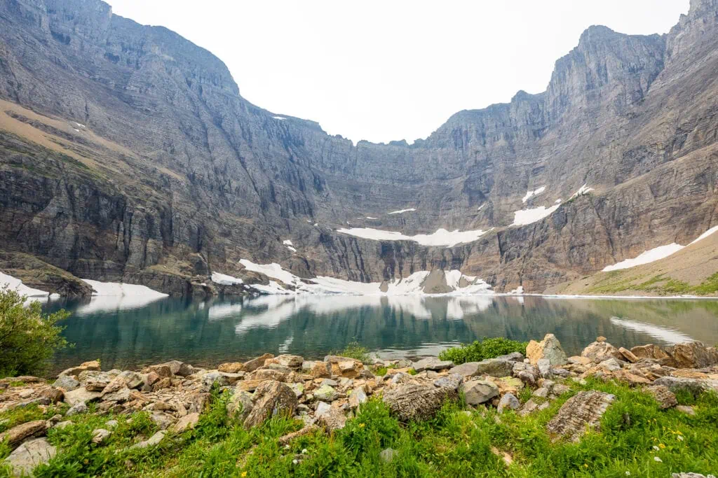 A bright overcast day at Iceberg Lake in the Many Glacier region of Glacier National Park. The water is turquoise blue and icebergs can be seen against the cliffs that surround the lake.