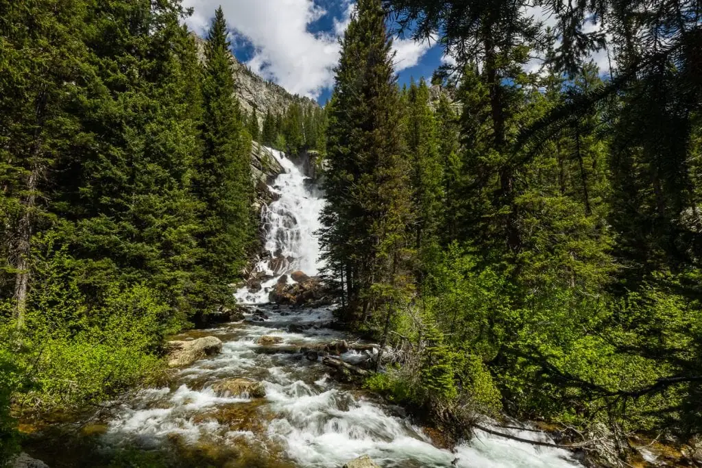 A landscape photo of Hidden Falls, a large waterfall located in a forest in Grand Tetons National Park.