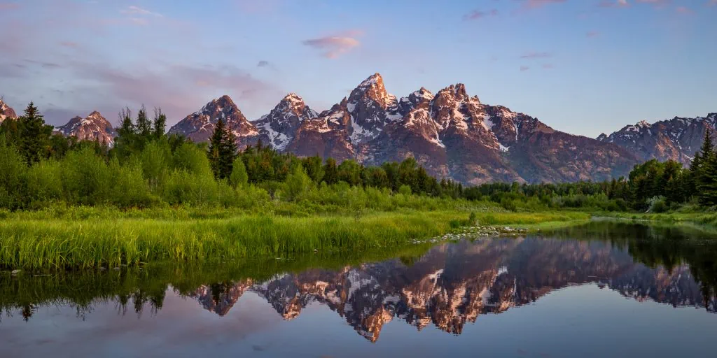 First light's purple and pink glow on the Tetons range in Wyoming in this colorful landscape photo at Schwabacher's Landing taken by Grand tetons elopement photographer Lucy Schultz.