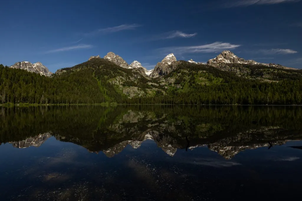 A mirror's reflection of the Grand Tetons mountain range in Taggart Lake on a summer's day.
