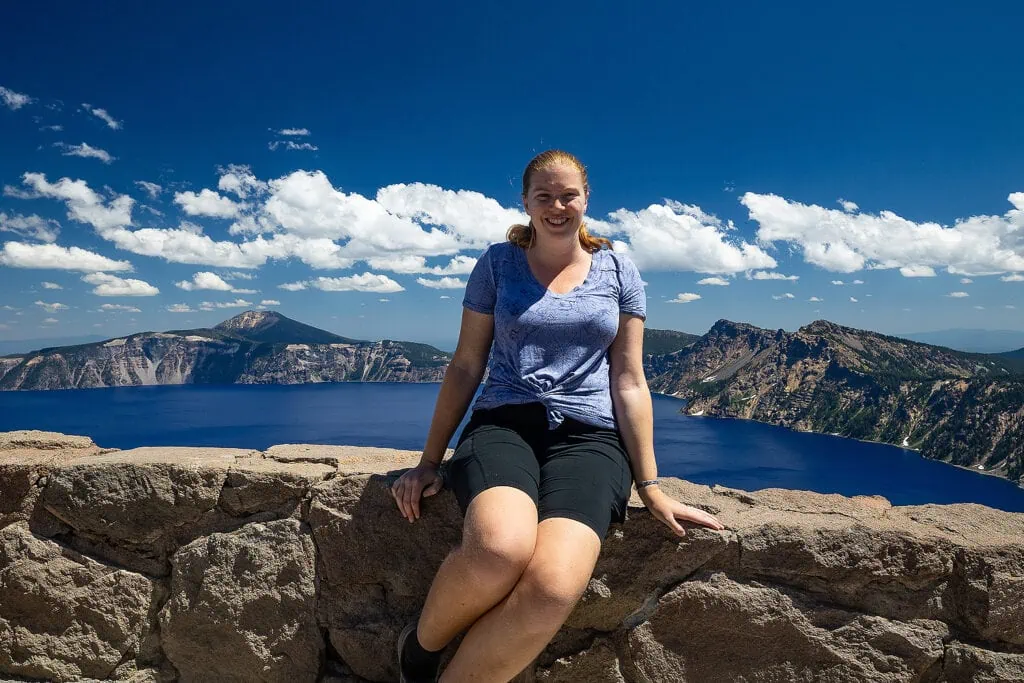 Crater Lake National Park elopement photographer Lucy Schultz sits on a stone wall overlooking crater lake.