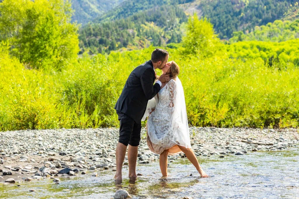 A couple wading into an icy river right after their elopement ceremony in the mountains of Colorado.