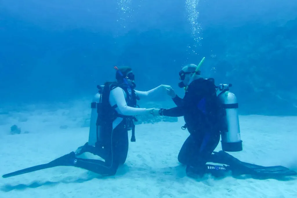 A couple kneels together on the ocean floor while scuba diving in Hawaii.