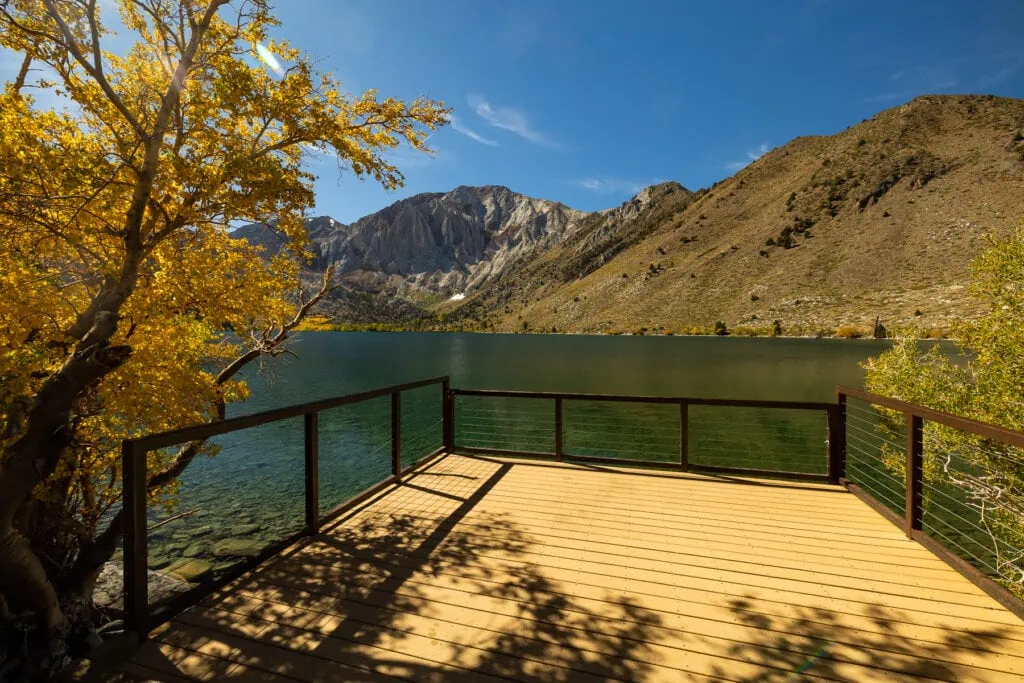 An ADA Accessible dock on Convict Lake in Mammoth Lakes, California, with fall trees on either side and mountains visible across the lake.
