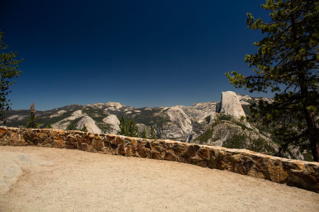 A low rock wall skirts Washburn Point, an ADA accessible view of Half dome on Glacier Point road in Yosemite National Park.